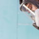 Worker wearing a full-face reusable respirator and hearing protection while using a handheld power tool in a dusty workspace.